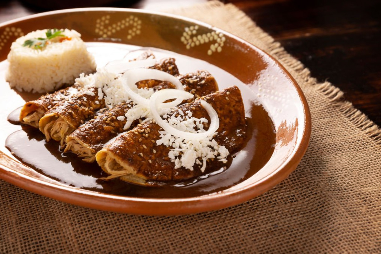 Mole negro enchiladas with rice and queso fresco on a clay plate